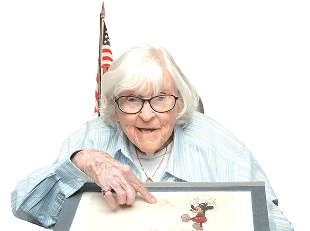 An older woman holding up a drawing of mickey mouse.