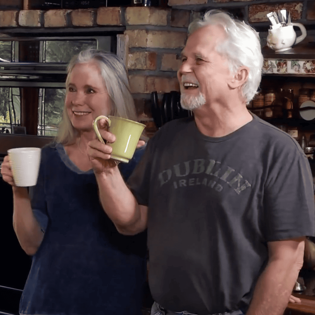 A man and woman standing in a kitchen holding coffee mugs.
