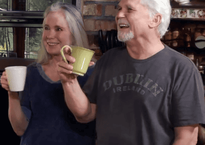 A man and woman standing in a kitchen holding coffee mugs.