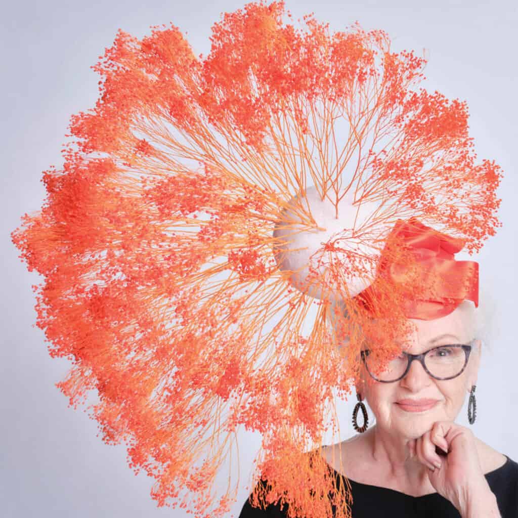 An older woman wearing glasses and an orange hat.