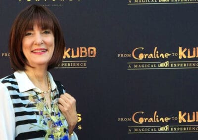 A woman in a striped blouse stands smiling at a "from coraline to kubo" promotional event backdrop.