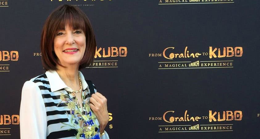 A woman in a striped blouse stands smiling at a "from coraline to kubo" promotional event backdrop.
